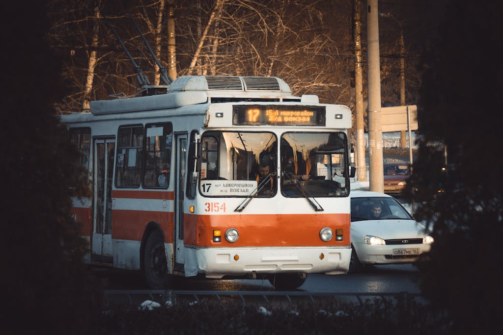 A classic red and white trolleybus on a city street during the day.