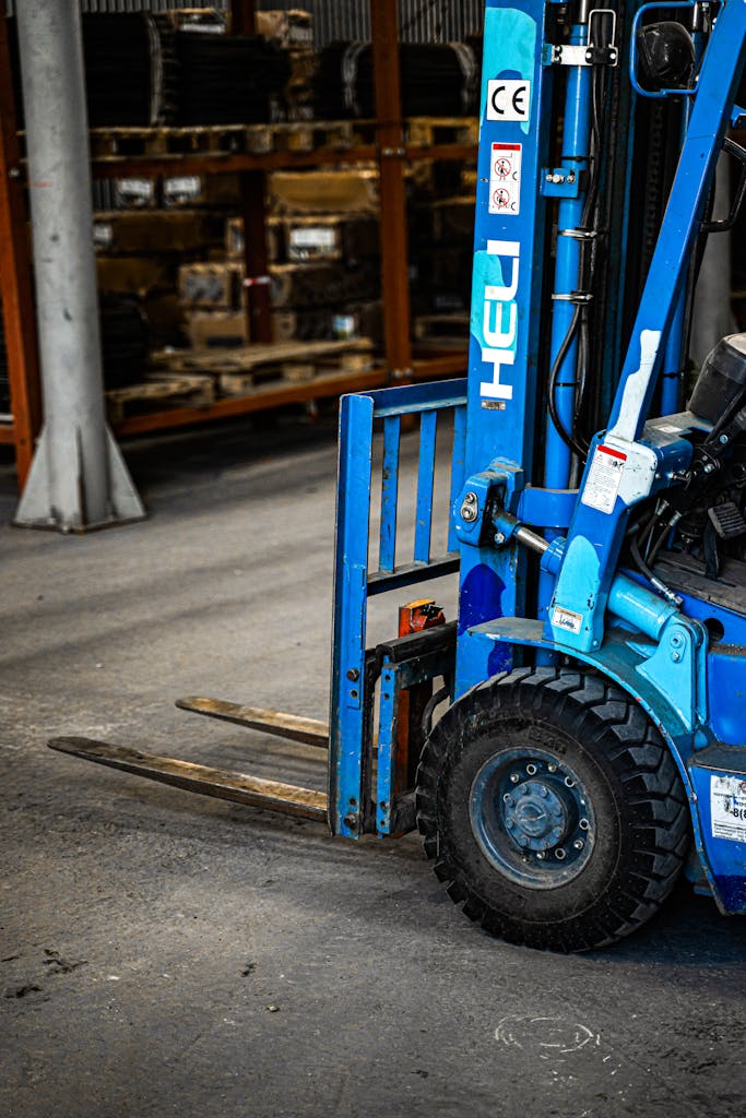 Blue forklift inside an industrial warehouse, parked near shelves with various items.