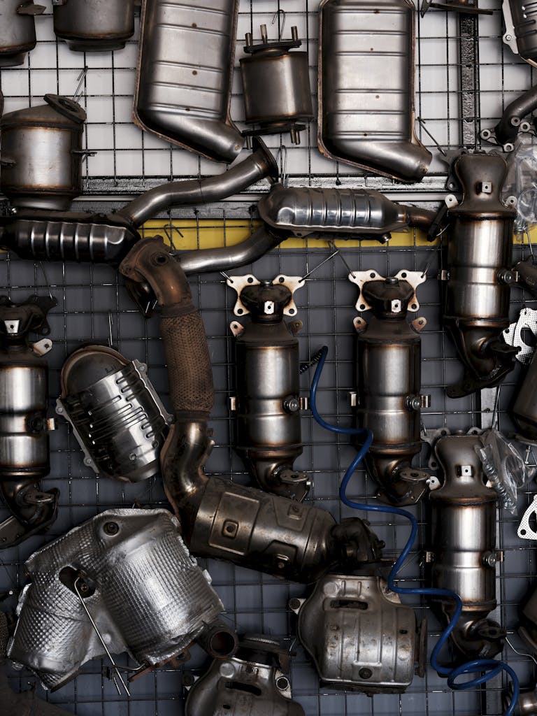 Collection of vintage car exhaust parts hanging in an industrial workshop setting.